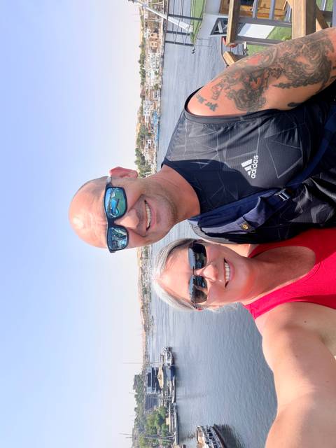 Couple takes a sunny selfie on a river boat with water and shoreline villages reflected in their sunglasses.