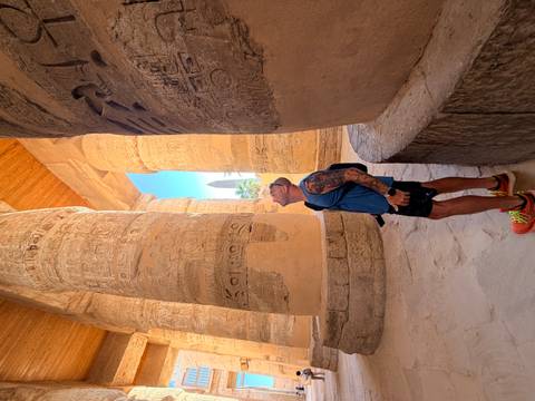 Traveler gazes upward at monumental hieroglyph-covered columns inside an ancient hall.