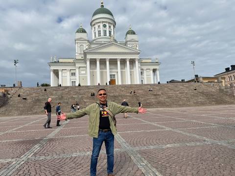 Man spreads arms joyfully in front of Helsinki Cathedral on spacious Senate Square.