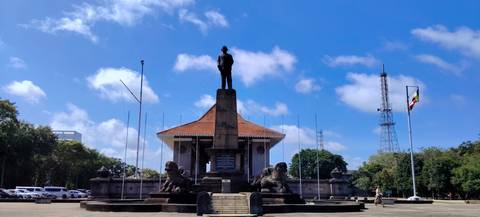 Statue-topped monument flanked by stone lions and flagpoles at Independence Square in Colombo under a bright sky.