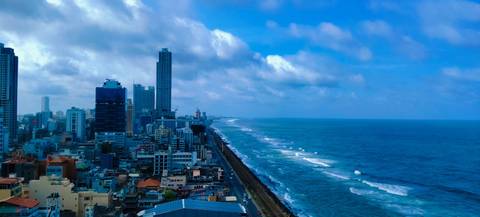 Elevated coastal skyline of Colombo with modern high-rises lining a long oceanfront highway beside turquoise waves.