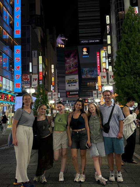 Group of young travelers posing on a neon-lit Tokyo street surrounded by bright billboards at night