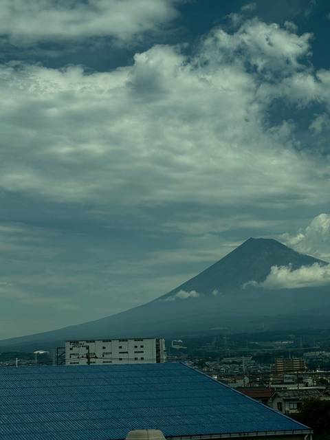 Silhouette of Mount Fuji’s cone peaks above low clouds against a muted teal sky