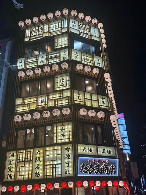 Night-time view of a multi-storey Japanese restaurant facade, lit by square lanterns and kanji signs.