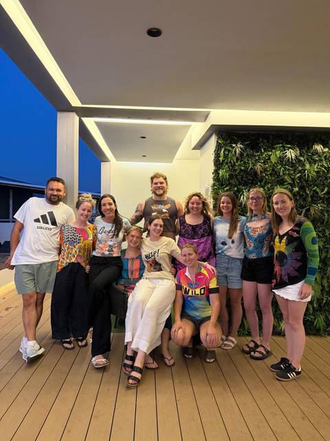 Large tour group gathers for an evening portrait on a terrace with a lush green wall backdrop.