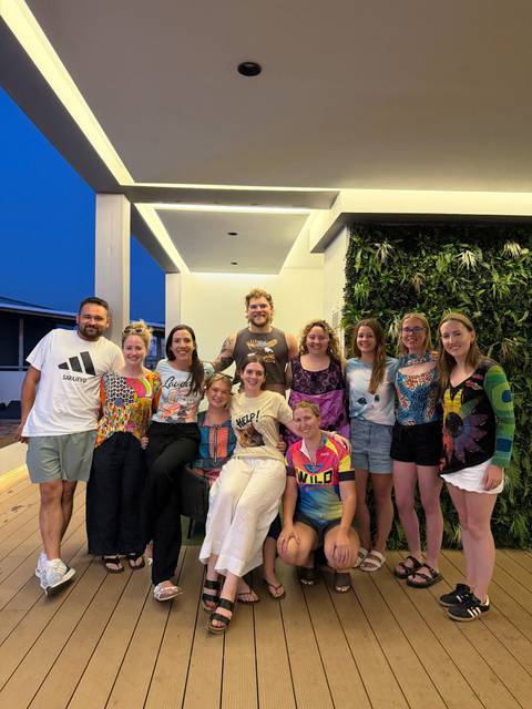 Large mixed group smiling for a posed photo on a modern terrace with a vertical garden wall at dusk.