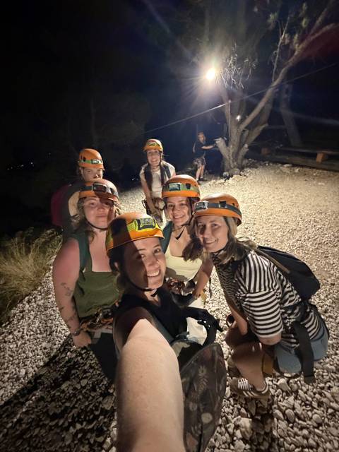Night-time selfie of friends in helmets and harnesses before an outdoor adventure.