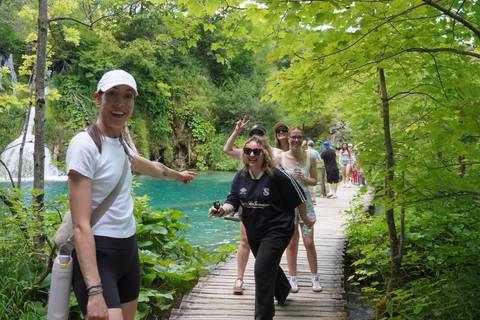 Happy travellers walking a wooden path over turquoise water and lush plants in a national park.
