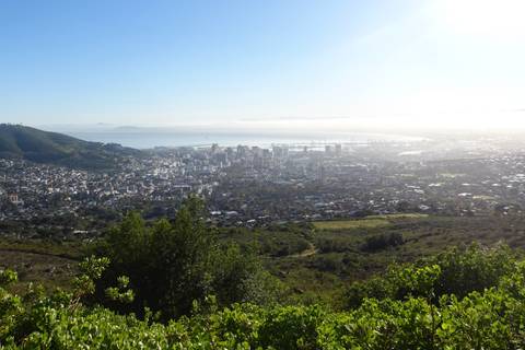 Wide panorama over a coastal city framed by mountains and a shining bay under clear skies.
