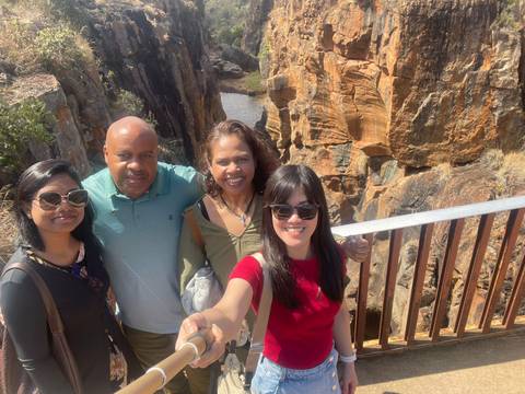 Four travellers taking a selfie on a viewing platform with rugged orange canyon walls behind them