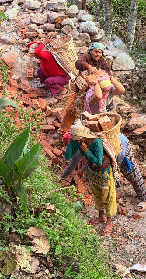 Women carrying baskets of bricks along a rocky slope during manual construction work.