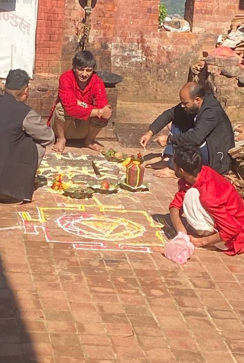 Small gathering creating colorful ritual drawings on a courtyard floor.