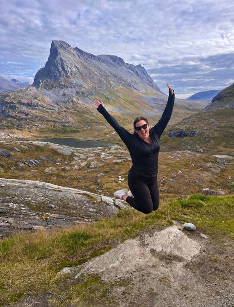 Joyful hiker leaps in the air atop a rocky slope overlooking Norwegian lakes and mountains.