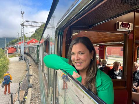 Smiling traveler leans out of a scenic train window on the Flåm Railway through fjord country.