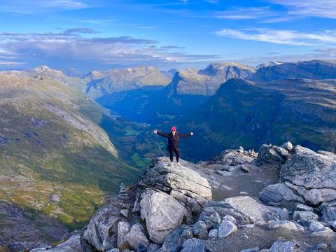 Traveler stands triumphantly on a rocky summit with sweeping views of deep valleys and peaks.