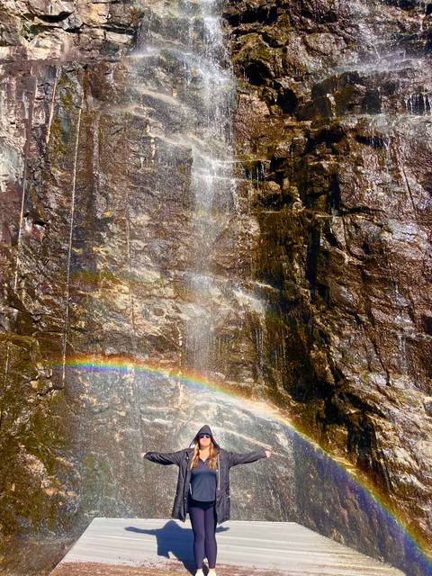 Close view of a rock face waterfall with mist creating a vibrant rainbow arc.