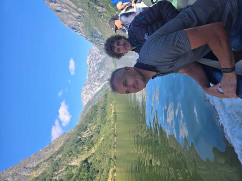 Two men enjoy a fjord boat ride with steep green mountains and blue water all around.