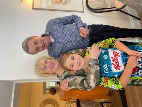 Smiling grandparents hug their granddaughter inside a bright home.