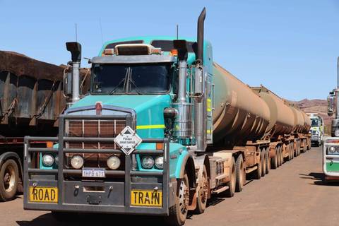 Long turquoise road-train truck with tanker trailers lined up at an outback depot under bright sun.