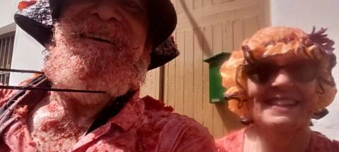 Close-up selfie of two participants covered in smashed tomatoes during La Tomatina festival.
