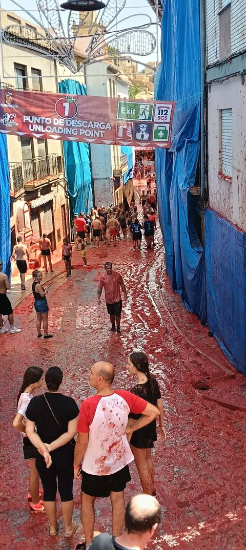 Narrow street coated in tomato pulp with festival-goers walking after La Tomatina event.