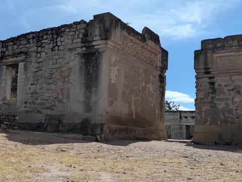 Stone walls and carved friezes of Mitla archaeological ruins under blue sky.