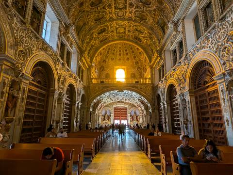 Lavish gold-decorated interior of a colonial church with visitors seated in pews.