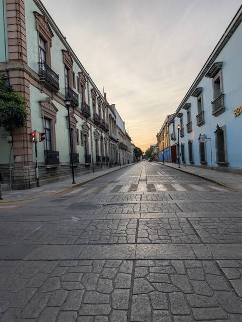 Empty cobblestone street in Oaxaca at dawn with historic buildings lining both sides.