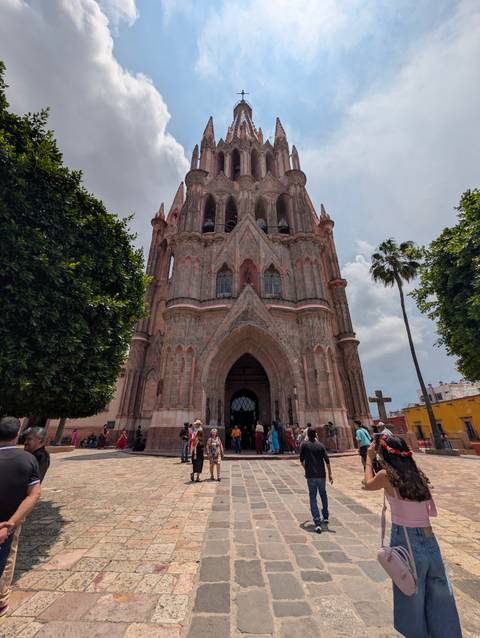 Neo-gothic pink stone Parroquia de San Miguel Arcángel towering above plaza crowd.