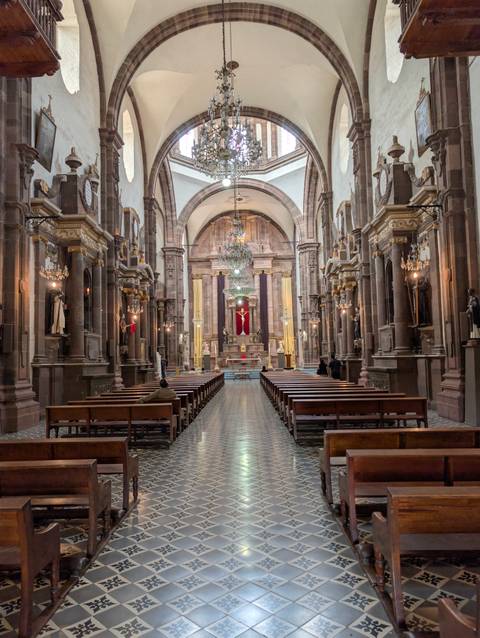 Ornate interior of colonial church with chandeliers and crucifix lit softly.