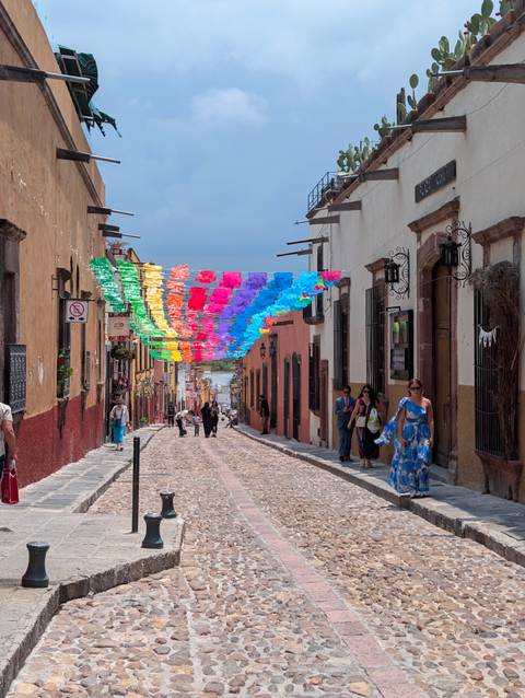 Colorful paper flags hanging above cobbled colonial street bustling with visitors in San Miguel.
