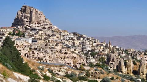 Panoramic view of Uchisar Castle towering above honey-colored stone houses carved into Cappadocian rock formations.
