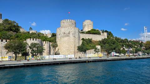 The massive stone walls and towers of Rumeli Fortress rise above the blue waters of the Bosphorus on a bright day.