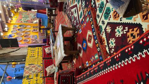 Vibrant Turkish rugs, cushions and low tables inside a traditional carpet shop or tea house.