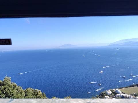 Expansive view over the deep-blue Bay of Naples with distant Mount Vesuvius, seen through a vehicle window.