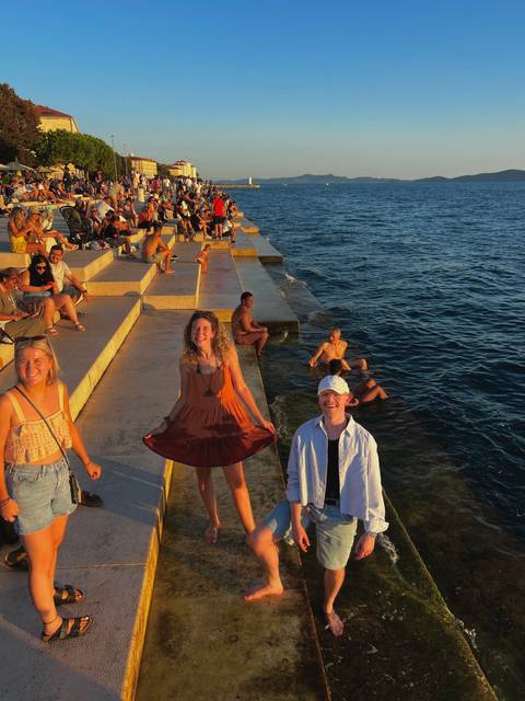 Crowds relax on sun-warmed stone steps beside the Adriatic Sea as waves splash below.