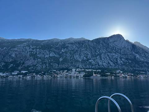 Steep grey cliffs loom above a tranquil bay with a small town reflected in calm water.