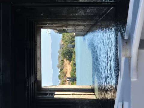 View from a boat inside a concrete lock chamber opening toward a calm river and hills.