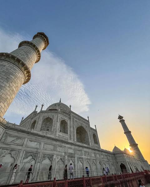 Upward angle of the Taj Mahal’s marble dome and minaret framed by a textured sky at dawn.