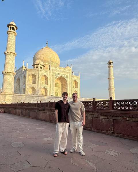 Two friends pose on the red sandstone terrace with the Taj Mahal glowing behind.