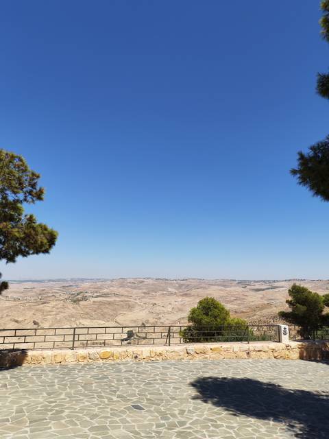 Panoramic view over arid rolling hills and distant villages beneath a cloudless sky.