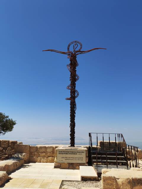 A tall bronze sculpture with spiral serpent motif rises against a clear blue sky.