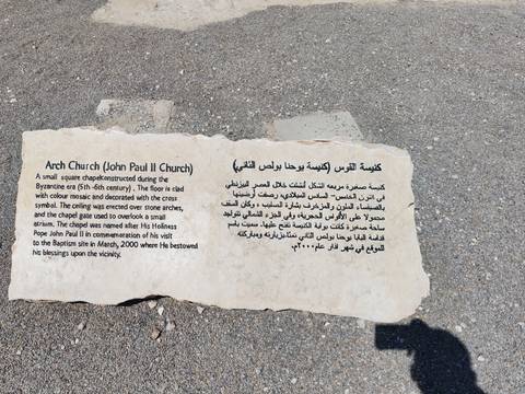 Broken stone sign on pavement describing the Arch Church (John Paul II Church) in English and Arabic.