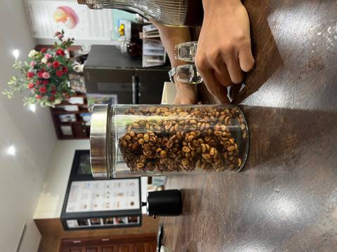 Glass jar filled with roasted coffee beans displayed on a wooden counter in a café setting.