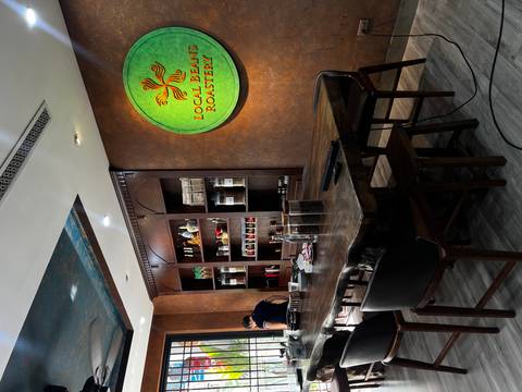 Interior of a boutique coffee roastery featuring wooden shelving, jars of beans, and a lit company logo sign.
