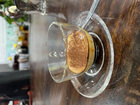 Glass cup of rich Vietnamese egg coffee served on a clear saucer atop a dark wooden table.
