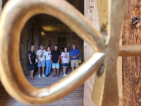 Tour group posing inside Abu Simbel temple viewed creatively through a decorative railing.