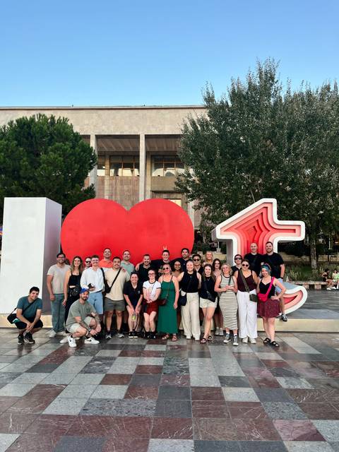 Large travel group posing in front of the red heart sculpture in Tirana city square.
