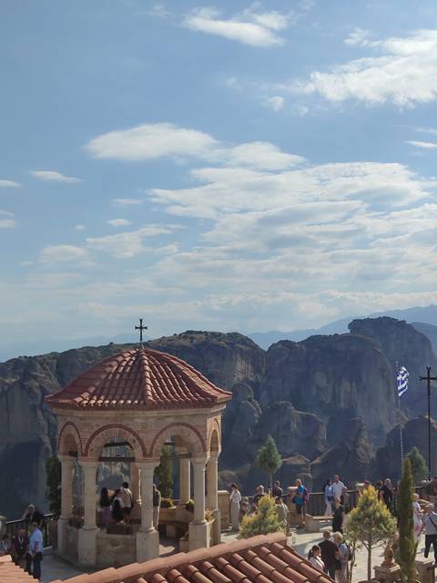 Tiled monastery rooftop and Greek flag with the towering rock pillars of Meteora beyond.