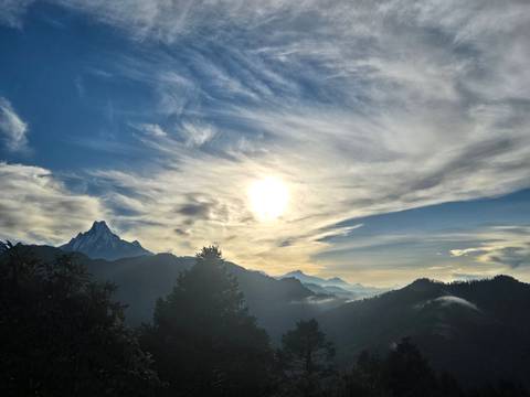 Dramatic sunrise over layered Himalayan peaks with the sun glowing through streaked clouds.